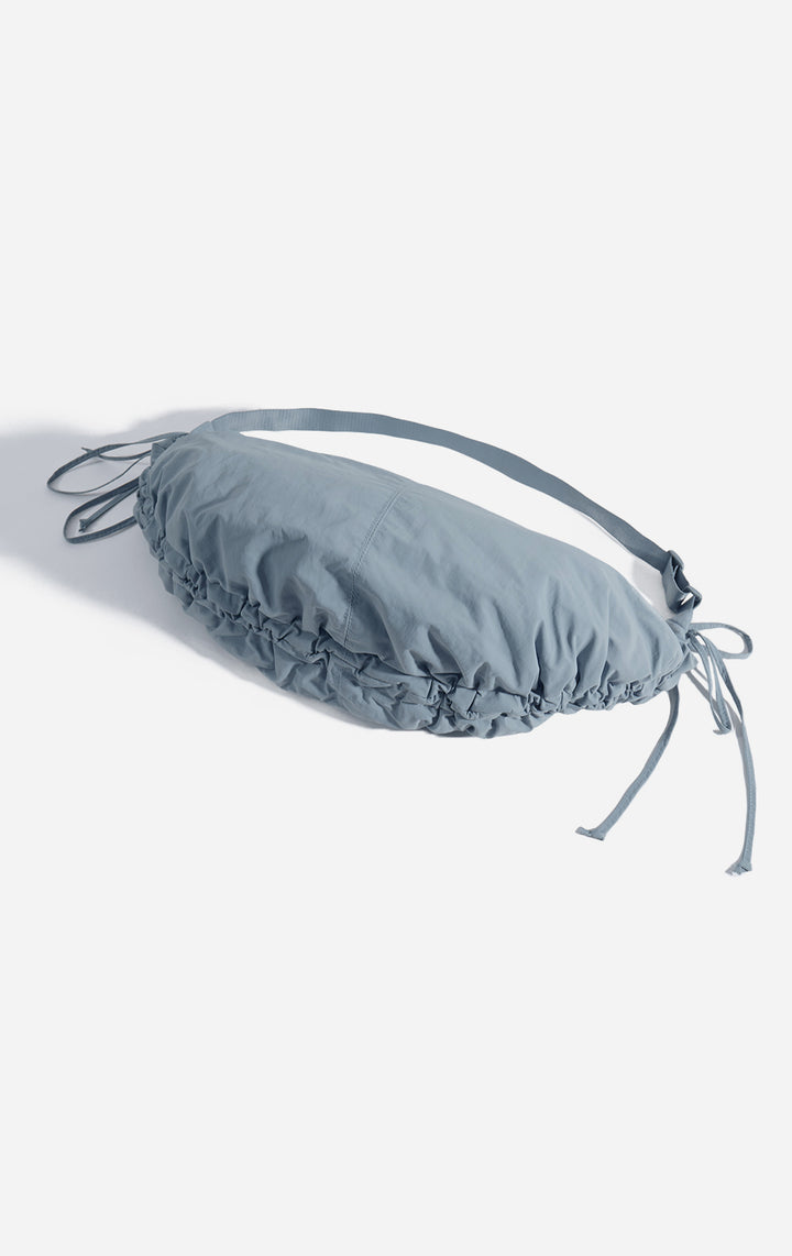 Stylized photo of the Blue Dumpling Shoulder Bag with Drawstring on minimal setup
