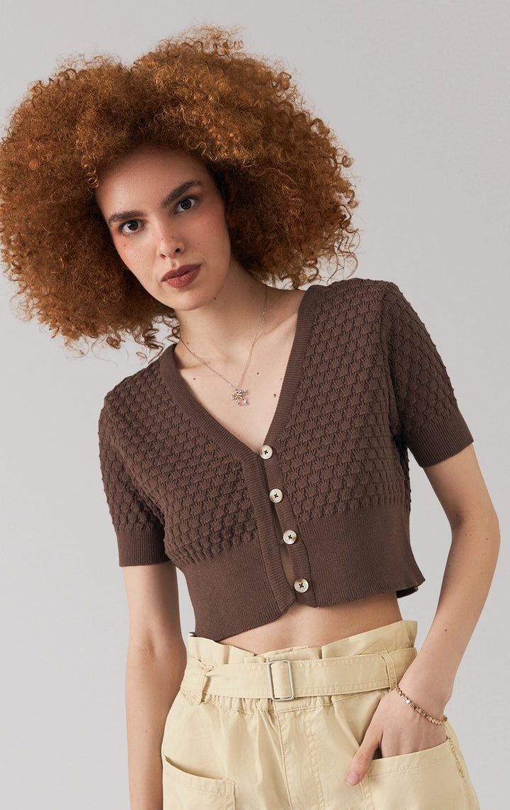 A stylized fashion photo of the pointelle knit button front crop top that is worn with bottoms and accessories by a model to see it in motion