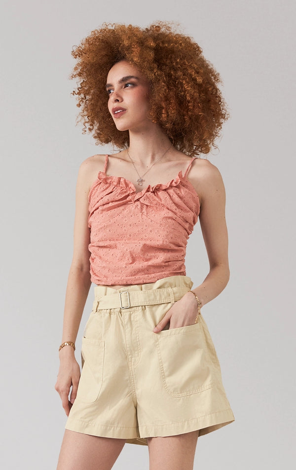 A stylized fashion photo of the eyelet draped top with ruffles that is worn with bottoms and accessories by a model to see it in motion